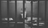 An out of focus bed seen through the bars of a jail cell