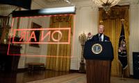 Joe Biden giving a speech at a podium with a large red "ON AIR" sign hanging in front of him