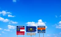 Road signs for the states Georgia, Pennsylvania and Arizona against a blue sky with clouds