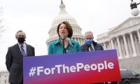 Amy Klobuchar infant of the U.S. capitol building standing behind a podium on which is a sign that read "#ForThePeople"