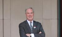 Trevor Potter posing with his arms folded in front of a wall and wearing an I Voted sticker on his lapel