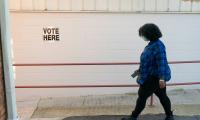 A woman walks by a sign that says "Vote Here".