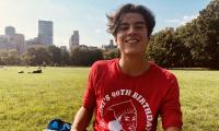 Michael Lieberman sitting outside on the grass with city buildings behind him