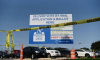 A sign that says "Deliver vote by mail application & ballot here" with caution tape in front of it.