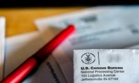 Close up of the return address on a census envelope with papers and a red pen out of focus in the background