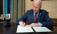 Joe Biden sitting at a desk signing a piece of paper