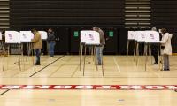 People voting at rows of voting booths in a school gym.