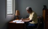 A man sitting at a desk in front of a window filling out a ballot.