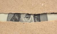 Benjamin Franklin's face on the one hundred dollar bill seen peeking out from behind two pieces of torn paper