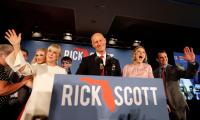 Rick Scott standing behind a podium with his name and an outline of the state of Florida on the front surrounded by several other people