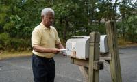 An African American man puts an envelope into a mailbox