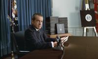 Nixon sitting at a desk in front of a microphone
