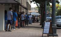 Voters stand in line on a sidewalk. There is a sign about where voters should park. 