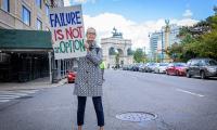 A woman standing in the middle of the street holding a sign that says "Failure Is Not An Option".