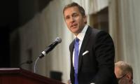 Eric Greitens speaking into a microphone at a podium.