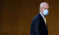 Sen. Ron Johnson, wearing a face mask, walks to the right side of the image.