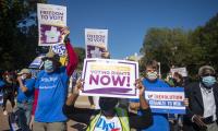 Demonstrators holding signs which say "Pass the Freedom to Vote Act" and "No more excuses. Voting right now!"