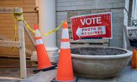 A sign which says "Vote, Photo ID Required" next to some caution tape and construction cones.