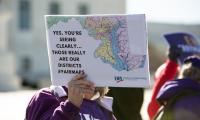 A women's hand holding a sign with a map of Maryland which says "Yes, you're seeing clearly...those really are our districts. #fairmaps"