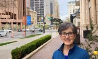 Wendy Martin standing on a brick sidewalk with an intersection and tall city buildings behind her