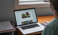 Over the shoulder shot of a woman looking at a laptop screen which is open to a web browser showing a page with videos and images.