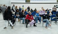 People sit on folding chairs in a gymnasium holding sign that say "Fair Maps NOW!"