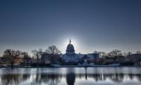 Brightly lit dawn sky behind the illuminated dome of the Capitol in Washington DC with the pool and statues