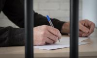 A man's hand holding a pen and writing behind bars