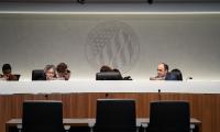 People sit behind a large desk with microphone in front of them and a large logo behind at the Federal Election 