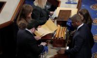 A top-down view of people in Congress opening a box containing manilla envelopes