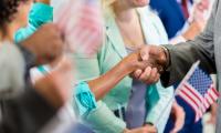 An anonymous man shakes an anonymous woman's hand in the middle of a crowd where people are holding American flags