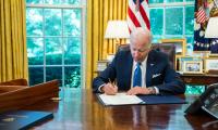 President Joe Biden sitting at his desk in the Oval Office signing a document