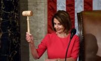 Nancy Pelosi standing at a podium raising a gavel and smiling