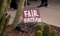 A sign saying "Fair Election" positioned among some cacti with the feet of people standing in line behind it
