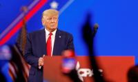 Donald Trump standing on a stage beside a podium with silhouettes of hands from a crowd in front of him