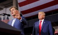 Do. Mehmet Oz speaking at a podium with Donald Trump standing directly behind him