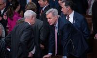 Kevin McCarthy leaning forward with his hands on a desk speaking with another man with other members of Congress around them