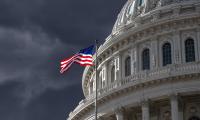 A close up of the dome of the U.S. Capitol Building with an American flag flying and a dark cloudy sky in the background