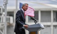 Bill de Blasio speaking at a podium with an American flag behind him