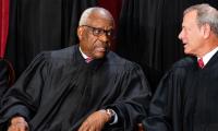 Clarence Thomas seated in black robes speaking with Chief Justice John Roberts