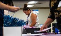 A woman bends over a table with boxes of ballots