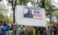 A person holds a sign featuring John Lewis, which says "Protect Our Vote" in front of the U.S. Capitol Building