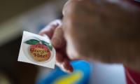 Hands holding a sticker with a peach on it that says "I'm a Georgia Voter"