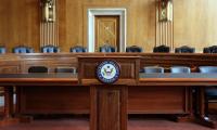 A podium with a microphone with the Senate seal on the front in front of two rows of chairs behind desks