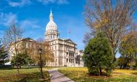 The Michigan state capitol building surrounded by trees on a sunny fall day