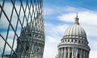 The dome of the Wisconsin capitol building next to its own reflection in the glass windows of an office building