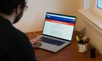 A man sitting at a laptop viewing a website with a banner that says "What Voters Need to Know"