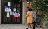 Two women walks towards double doors with signs on them that say "Polling Place, Vote Here"