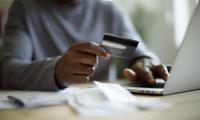 A man holds a credit card while typing on a laptop