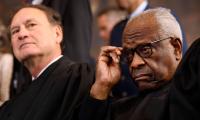 Clarence Thomas adjusting his glasses with Samuel Alito in the background behind him.